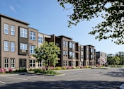 Thumbnail 5 of 21 - A row of brown apartment buildings with trees and flowering bushes in front.