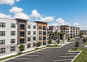 Thumbnail 11 of 60 - A row of modern apartment buildings with a parking lot in front.