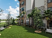 Thumbnail 8 of 60 - A large grassy area in front of a building with a bench and a tree.