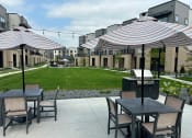 Thumbnail 25 of 58 - a patio with tables and umbrellas and a lawn in front of apartments at Meridian at CityPlace in Woodbury, MN 55125
