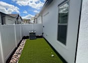 Thumbnail 7 of 17 - A white fence separates a small grassy area from a white house.