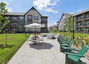 Thumbnail 77 of 88 - an outdoor patio with tables and chairs and an umbrella in front of an apartment building at The Depot Raymore, MO 64083