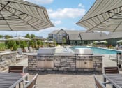 Thumbnail 63 of 88 - a resort style pool with a grill and umbrellas at The Depot Raymore, MO 64083