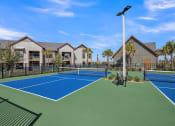 Thumbnail 19 of 30 - two tennis courts with apartments in the background at Canter, Ocala, FL