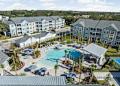 Thumbnail 1 of 36 - A large swimming pool surrounded by palm trees and lounge chairs in front of apartment buildings.