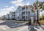 Thumbnail 8 of 36 - A large apartment complex with a parking lot in front.