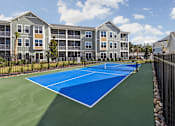 Thumbnail 27 of 36 - A tennis court is in front of a building with apartments.