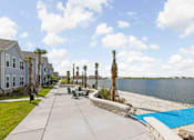 Thumbnail 73 of 83 - A view of a walkway with a pool and palm trees. at Junction Apartments in Rockledge, FL
