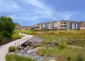 Thumbnail 2 of 40 - a bridge over a creek in front of an apartment building at Watermark on Twenty Mile, CO