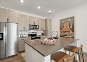 Thumbnail 49 of 108 - a kitchen with stainless steel appliances and a large island with bar stools at The Maddox Luxury Apartment Homes, Buckeye Arizona  