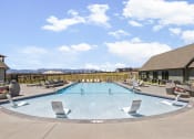 Thumbnail 28 of 38 - an outdoor pool with chairs and tables and a building with mountains in the background at Upland Flats, Colorado Springs, CO, 80922