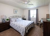 Thumbnail 6 of 16 - A bedroom with a bed, nightstand, chair, and window.