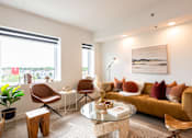 Thumbnail 4 of 36 - A living room with a brown sofa, a glass table, and a painting on the wall.