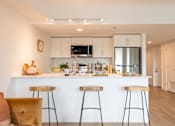Thumbnail 7 of 36 - A modern kitchen with white cabinets and a white island with three bar stools.