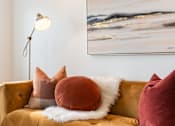 Thumbnail 16 of 36 - A painting hangs on a wall above a couch with pillows and a fur throw.