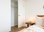 Thumbnail 21 of 36 - A bedroom with a bed, a nightstand with a candle, and a door leading to a closet.