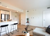 Thumbnail 5 of 47 - A living room with a white couch and a bar area with stools.