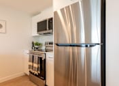 Thumbnail 10 of 47 - A stainless steel refrigerator stands in a kitchen with white cabinets and a microwave above the stove.