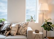 Thumbnail 11 of 47 - A living room with a grey sofa, a white lamp, and a green plant.