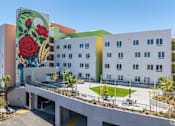 Thumbnail 2 of 15 - A mural of a red rose is painted on the side of a white building.