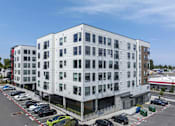 Thumbnail 11 of 24 - A large white building with a parking lot in front.