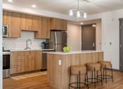 Thumbnail 14 of 20 - A kitchen with wooden cabinets and a counter with three stools at Elevation16 Apartments, Washington