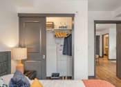 Thumbnail 15 of 20 - A bedroom with a bed, nightstand, and a closet with clothes hanging at Elevation16 Apartments, Seattle, WA, 98146