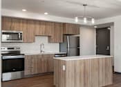 Thumbnail 4 of 20 - White Center, WA Studios For Rent - Elevation16 - Kitchen With Stainless Steel Appliances, Vinyl Plank Flooring, Kitchen Island, and Generous Kitchen Storage With Hardwood Cabinets