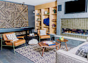 Thumbnail 39 of 68 - Cozy communal lounge in the apartment complex featuring stylish seating arrangements, a modern flat-screen TV, a warm fireplace, and a tabletop shuffleboard for residents to enjoy.