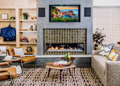 Thumbnail 44 of 68 - Cozy communal lounge in the apartment complex featuring stylish seating arrangements, a modern flat-screen TV, a warm fireplace, and a tabletop shuffleboard for residents to enjoy.