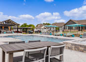 Thumbnail 12 of 23 - A poolside table and chairs are set up in front of a pool.
