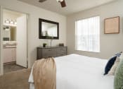 Thumbnail 22 of 39 - a bedroom with a white bed and a dresser and a bathroom at Stoneridge Apartments, Gainesville, FL