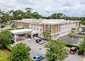 Thumbnail 1 of 5 - A parking lot with cars and a building with a red car in front.