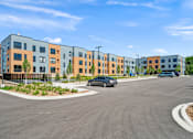 Thumbnail 34 of 36 - A modern apartment complex with a parking lot in front.