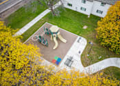 Thumbnail 22 of 23 - A playground with a slide and swings surrounded by trees with yellow leaves.