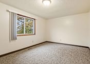 Thumbnail 15 of 23 - A room with a carpeted floor and a window with a view of trees outside.