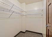 Thumbnail 11 of 23 - A walk-in closet with white shelves and a brown door.