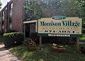 Thumbnail 7 of 9 - A sign for Morrison Village Apartments is in front of a brick building.