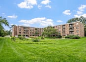 Thumbnail 9 of 25 - a large brick apartment building with green grass and trees