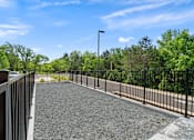 Thumbnail 35 of 36 - A gravel parking lot with a metal fence and trees in the background.