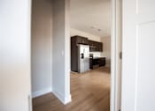 Thumbnail 18 of 47 - A kitchen with white walls and wooden floors is visible through an open door.