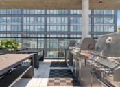 Thumbnail 21 of 35 - an outdoor patio with barbecue grills and picnic tables with a large building in the background