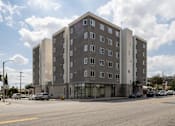 Thumbnail 7 of 19 - A large grey building with many windows sits on a street corner.