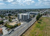 Thumbnail 4 of 19 - A large grey building is situated on a road with a yellow building to the left.