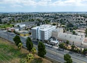 Thumbnail 1 of 19 - A white building with a blue stripe is in the center of a city street.