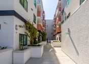 Thumbnail 16 of 17 - A long, narrow walkway between two buildings with a green exit sign on the wall.