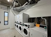 Thumbnail 11 of 19 - A row of industrial washing machines are installed in a laundry room.
