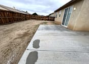 Thumbnail 2 of 10 - A backyard with a concrete patio and a wooden fence.