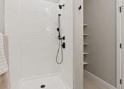 Thumbnail 1 of 21 - A white tiled shower with a black shower head and hand held shower.