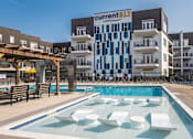 Thumbnail 23 of 60 - A pool with white chairs and a building with a sign that says "current 812" in the background.